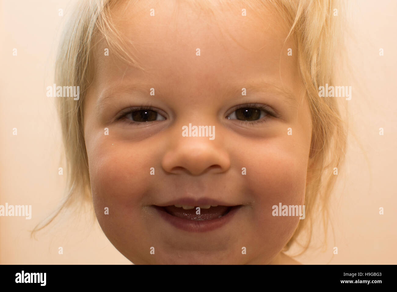 1 year old blond girl looking directly into camera with cheeky grin and brown eyes Stock Photo