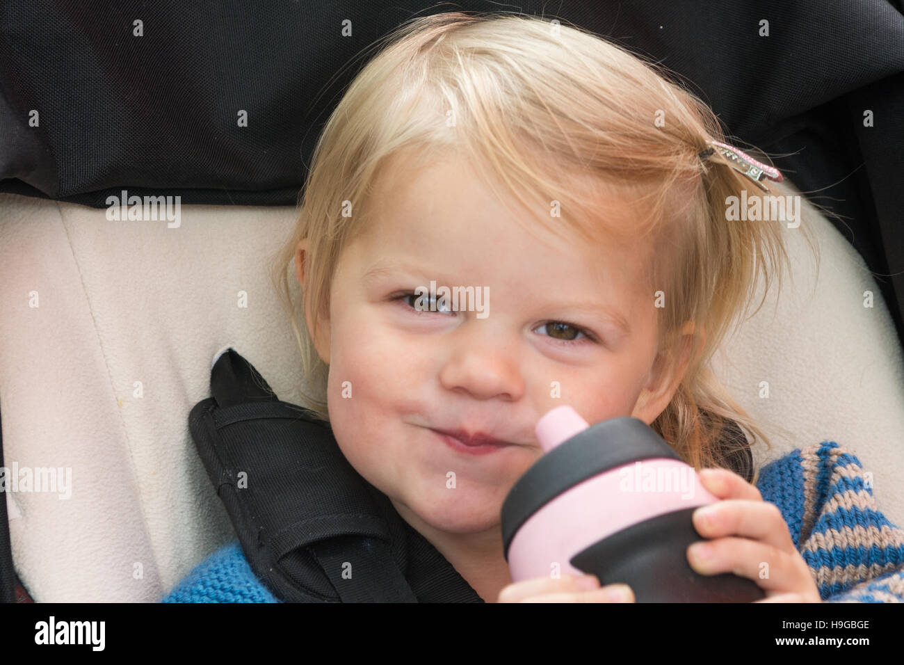 2 year old girl with blond hair with pink and black water bottle and cheeky grin Stock Photo