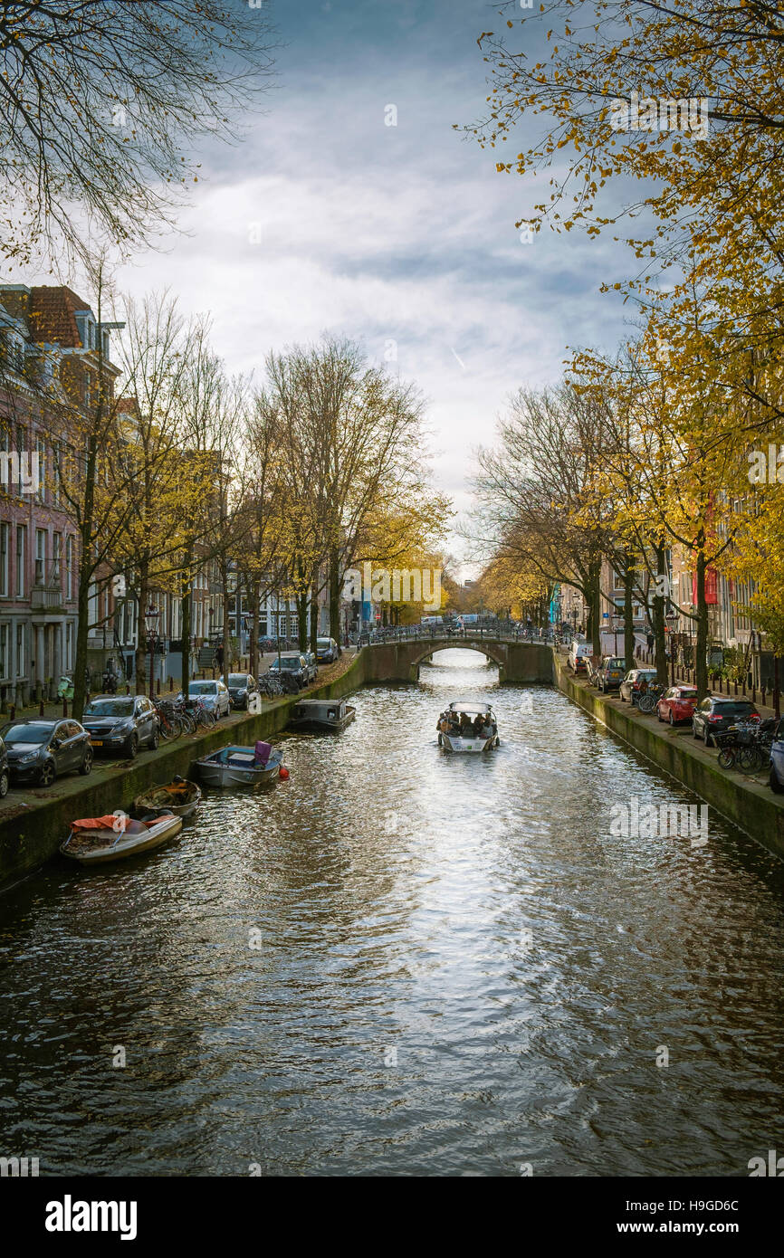 A small tourist boat sails up the Leidsegracht under autumn light, Amsterdam. Stock Photo