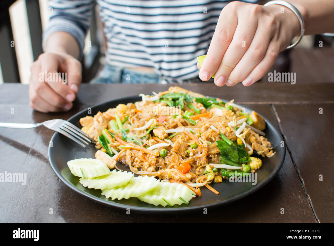 Female hand squeezing lime on Pad Thai in restaurant Stock Photo