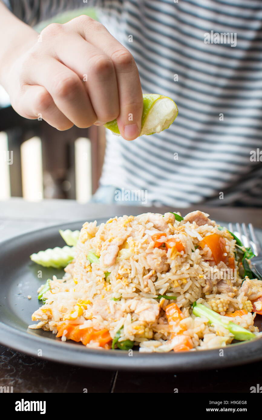 Female hand squeezing lime on fried rice meal Stock Photo