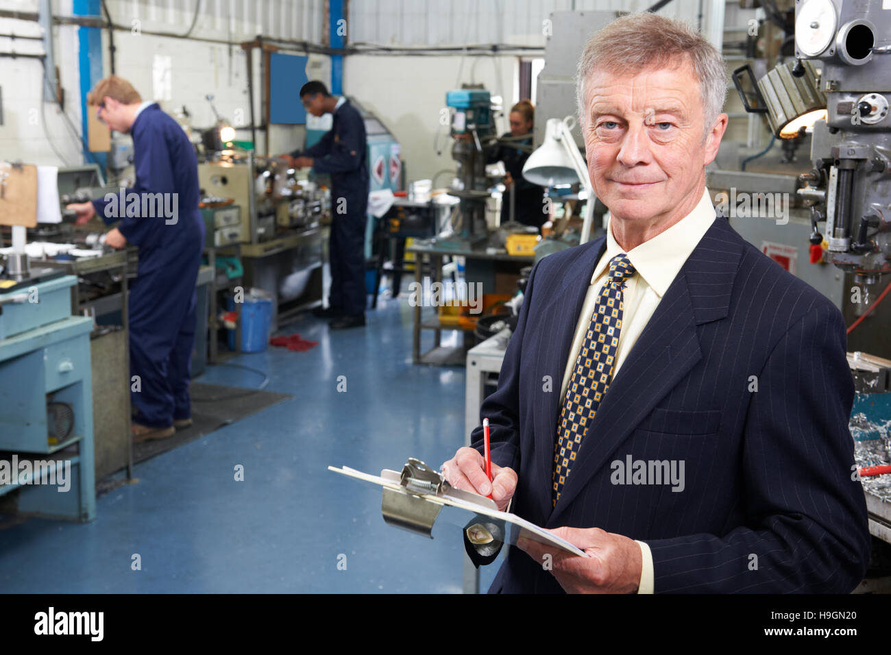 Owner Of Engineering Factory With Staff In Background Stock Photo