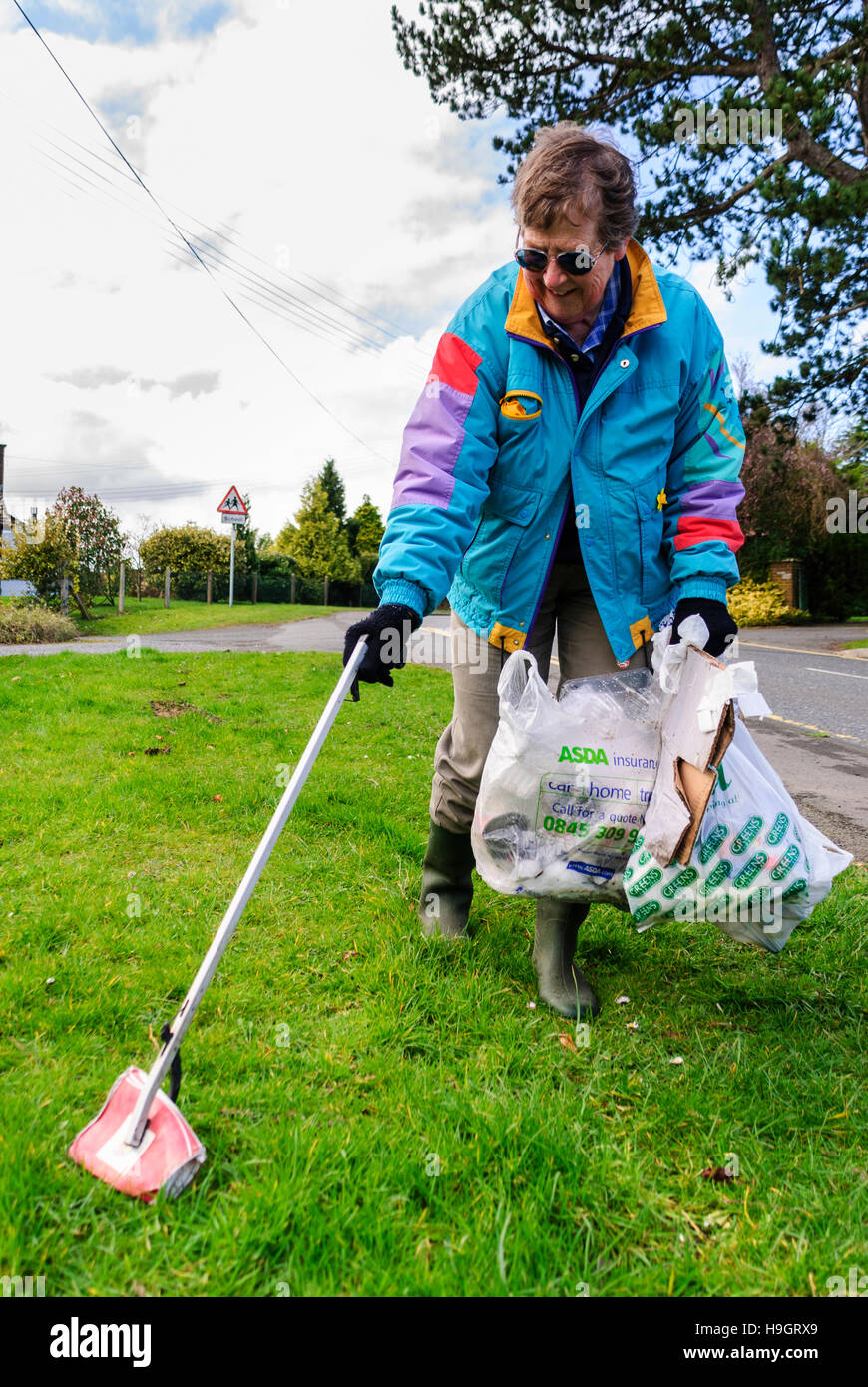 A woman uses a grabber to pick litter into bags. Stock Photo