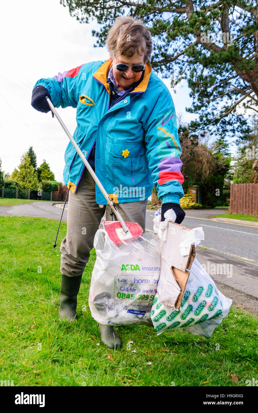 A woman uses a grabber to pick litter into bags. Stock Photo