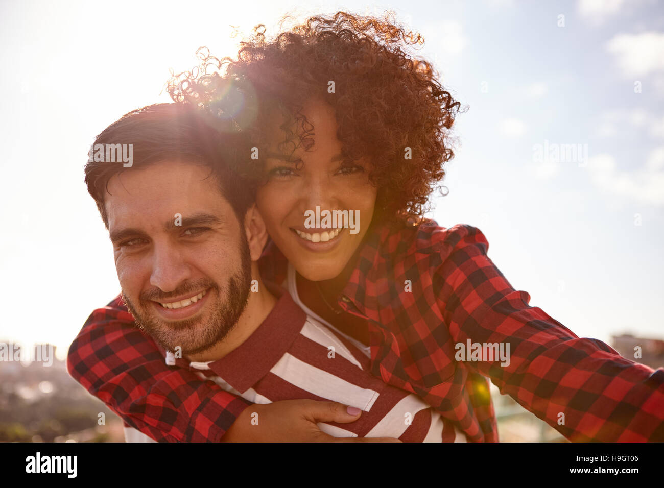 Close up of handsome young millennial couple with beautiful toothy smiles looking straight at the camera with the sun behind them Stock Photo
