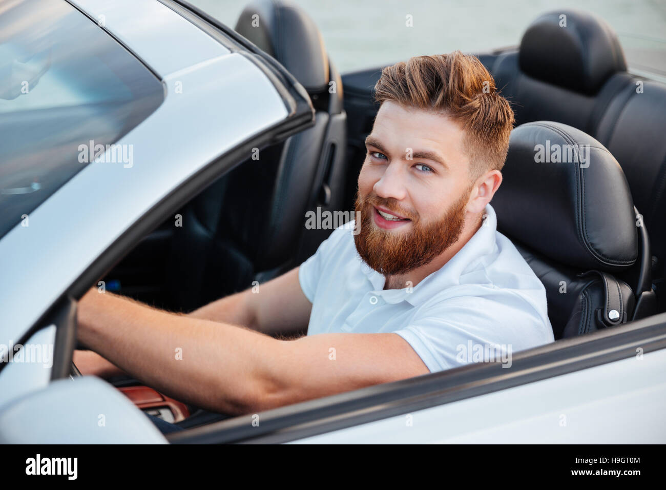 Happy young man driving cabriolet and looking at camera Stock Photo