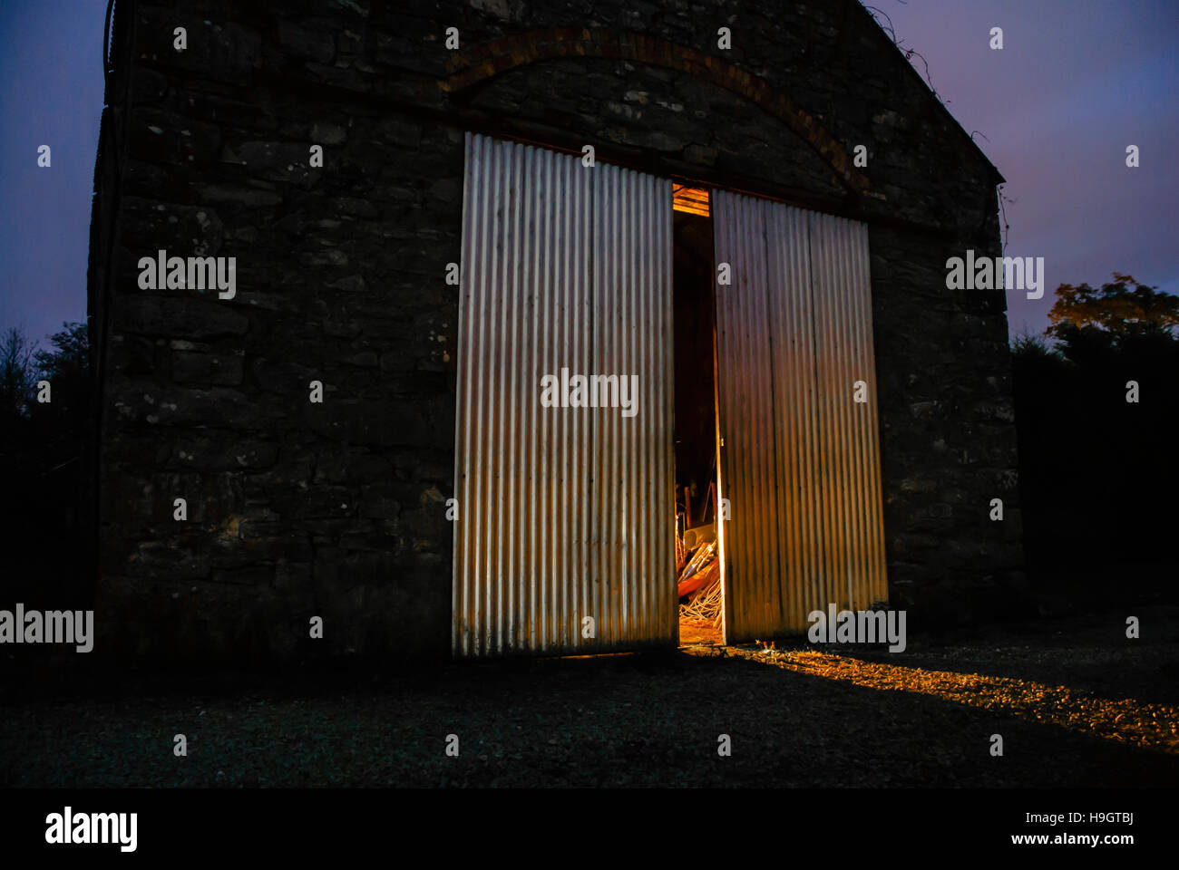 Light shines out from half open doors of an old Irish stone barn at night Stock Photo