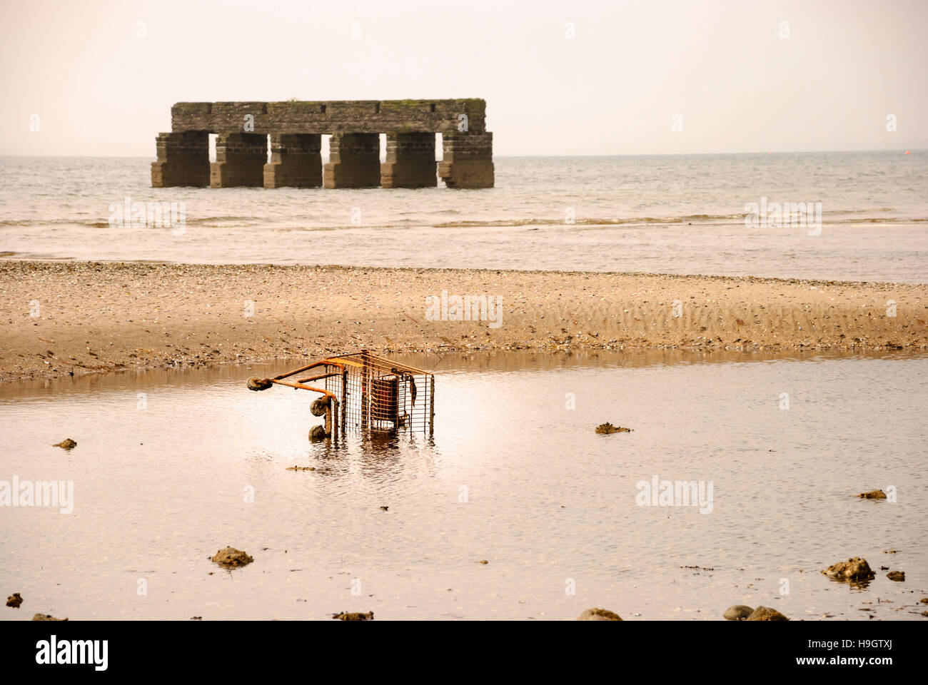 Rusty supermarket trolley cart lies half submerged in the sea. Stock Photo