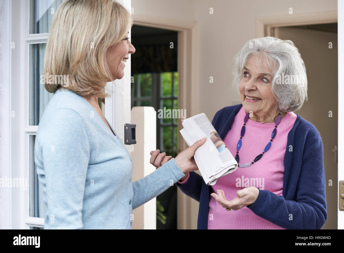 Woman Delivering Newspaper To Elderly Neighbour Stock Photo