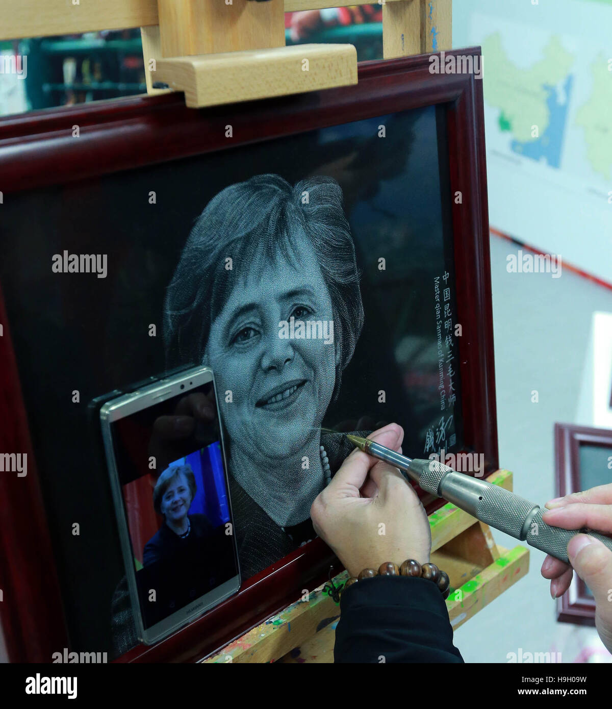 (161123) -- DUSSELDORF, Nov. 23, 2016 (Xinhua) -- Chinese artist Qian Sanmao makes a stone painting of German Chancellor Angela Merkel in Kunming exhibition container in Dusseldorf, Germany, Nov. 21, 2016. Some 15 containers have been unveiled under Dusseldorf's landmark, the over-200-meter-high telecommunications tower Rheinturm, to showcase cultural artifacts from the countries along the 'Belt and Road' routes. Launched Monday night under the title of 'Blue Containers' on New Silk Road, the event will last six days and see paintings, handicrafts, and musical instruments, among others, on dis Stock Photo