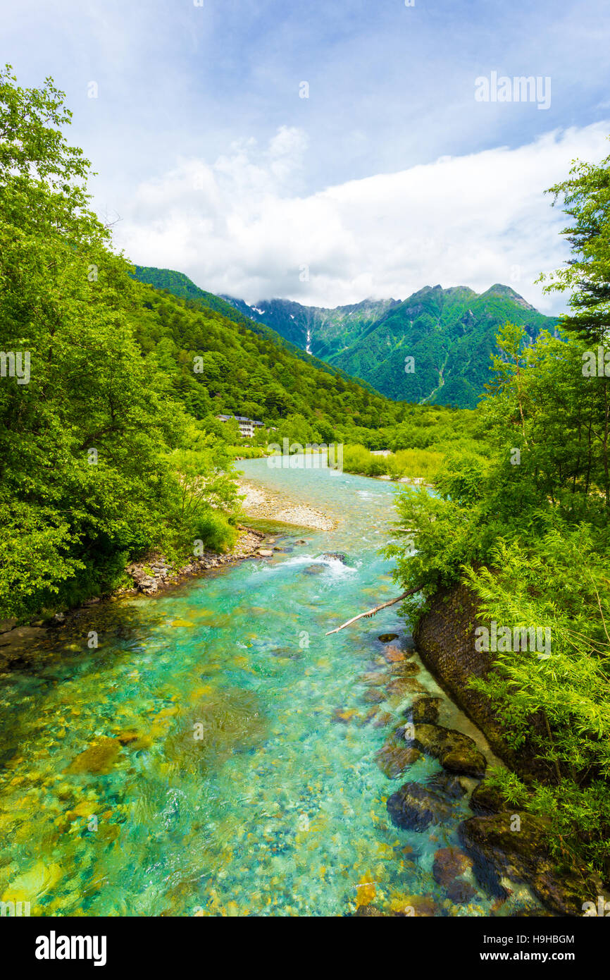 The crystal clear water of the Azusa river winds thru pristine forest with  landscape view of Mount Hotaka-Dake in Kamikochi Stock Photo