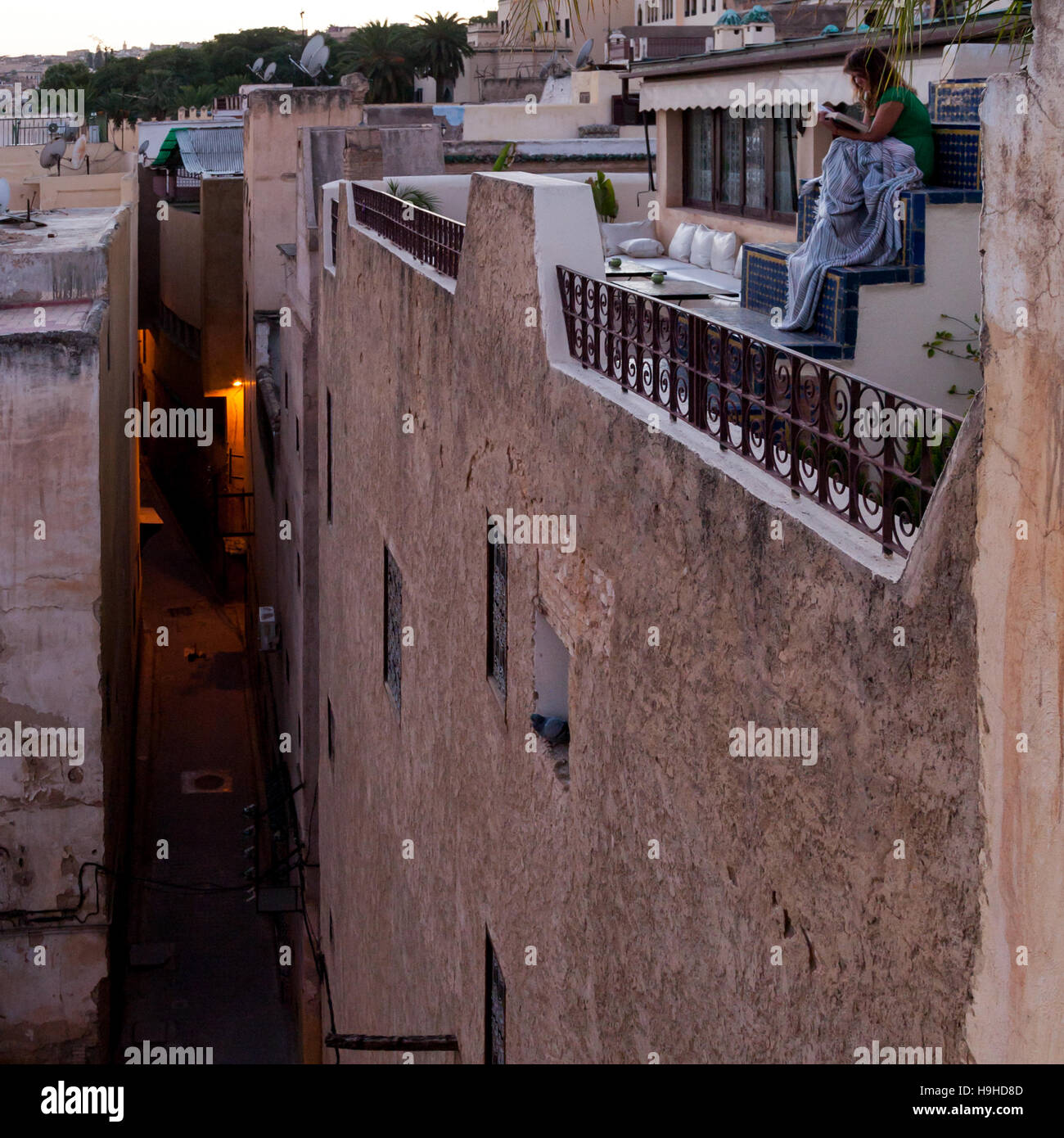 Young woman reading book on a riad roof patio in Fès, Morocco, at sunset Stock Photo