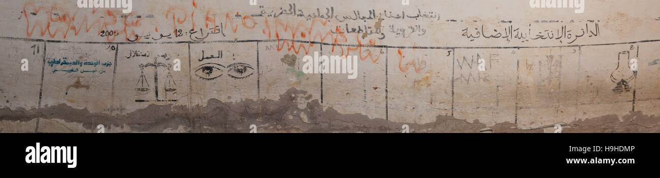 Election campaign notices for several political parties cover a wall in Fès, Morocco, written in Arabic and accompanied by handwritten additions and symbols such as a scale and an eye. Stock Photo
