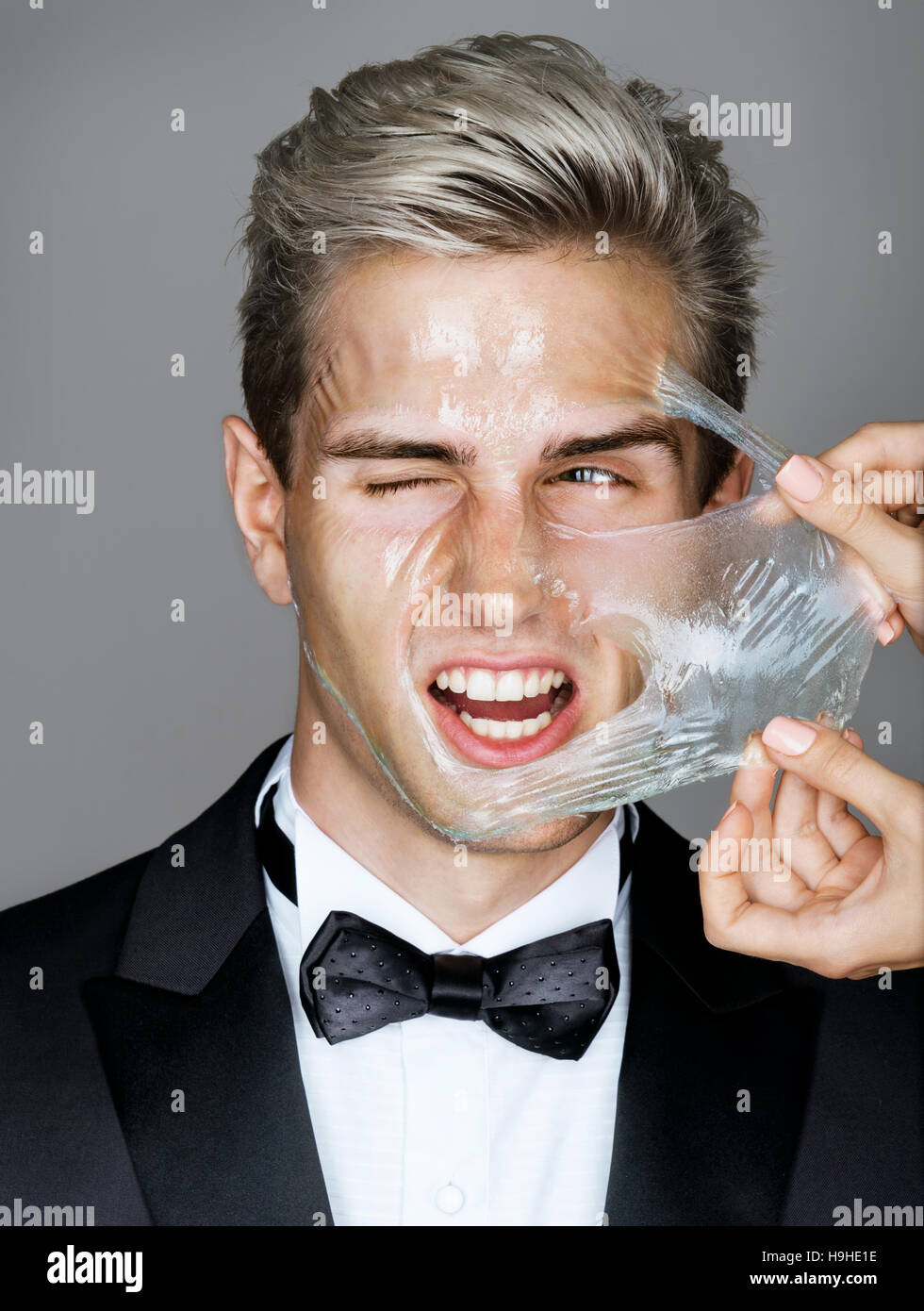 Pain. Elegant man in black suit removes peeling off a facial mask. Photo disaffected rich man on gray background. Skin care concept Stock Photo