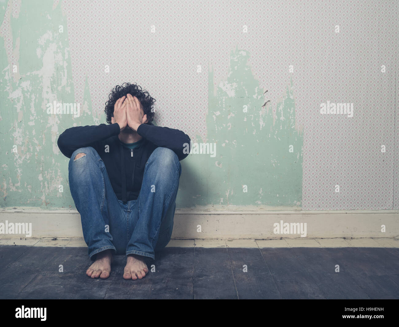 A sad and depressed young man is sitting on the floor in an empty room