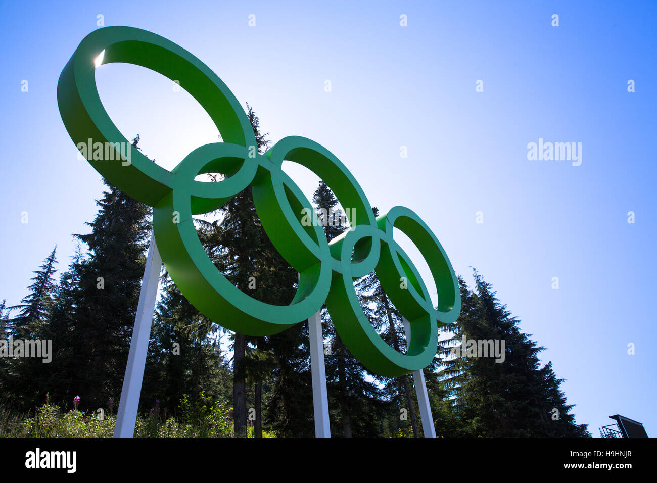Green Olympic Rings against blue sky and green trees inside the Vancouver Olympic Village - Vancouver, BC Stock Photo