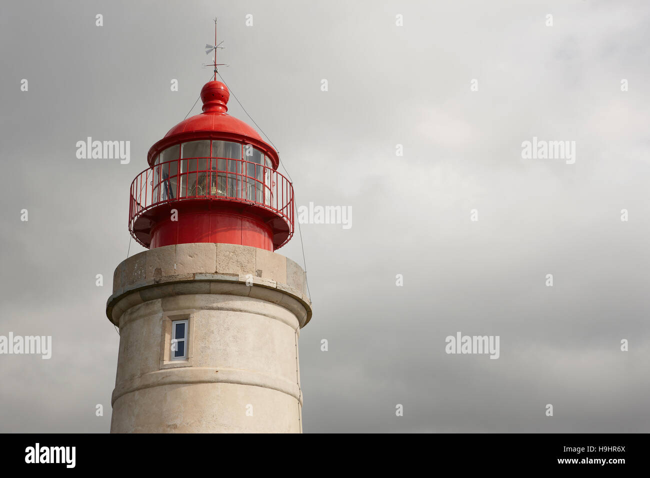 Stone lighthouse with metallic red dome on a cloudy day. Horizontal Stock Photo