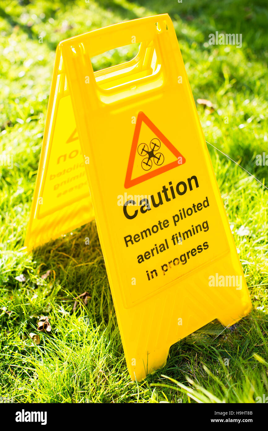 A Frame safety sign warning of drone operators filming. The sign reads 'Caution. Remote piloted aerial filming in progress'. Stock Photo
