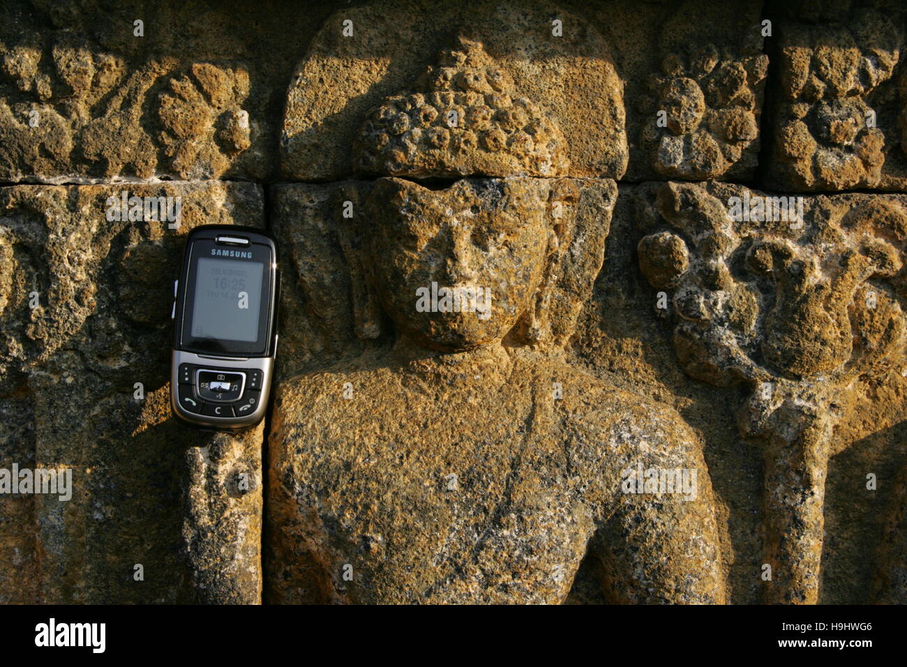 a relief Buddah holds a mobile phone at Borobudur in central Java, Indonesia Stock Photo