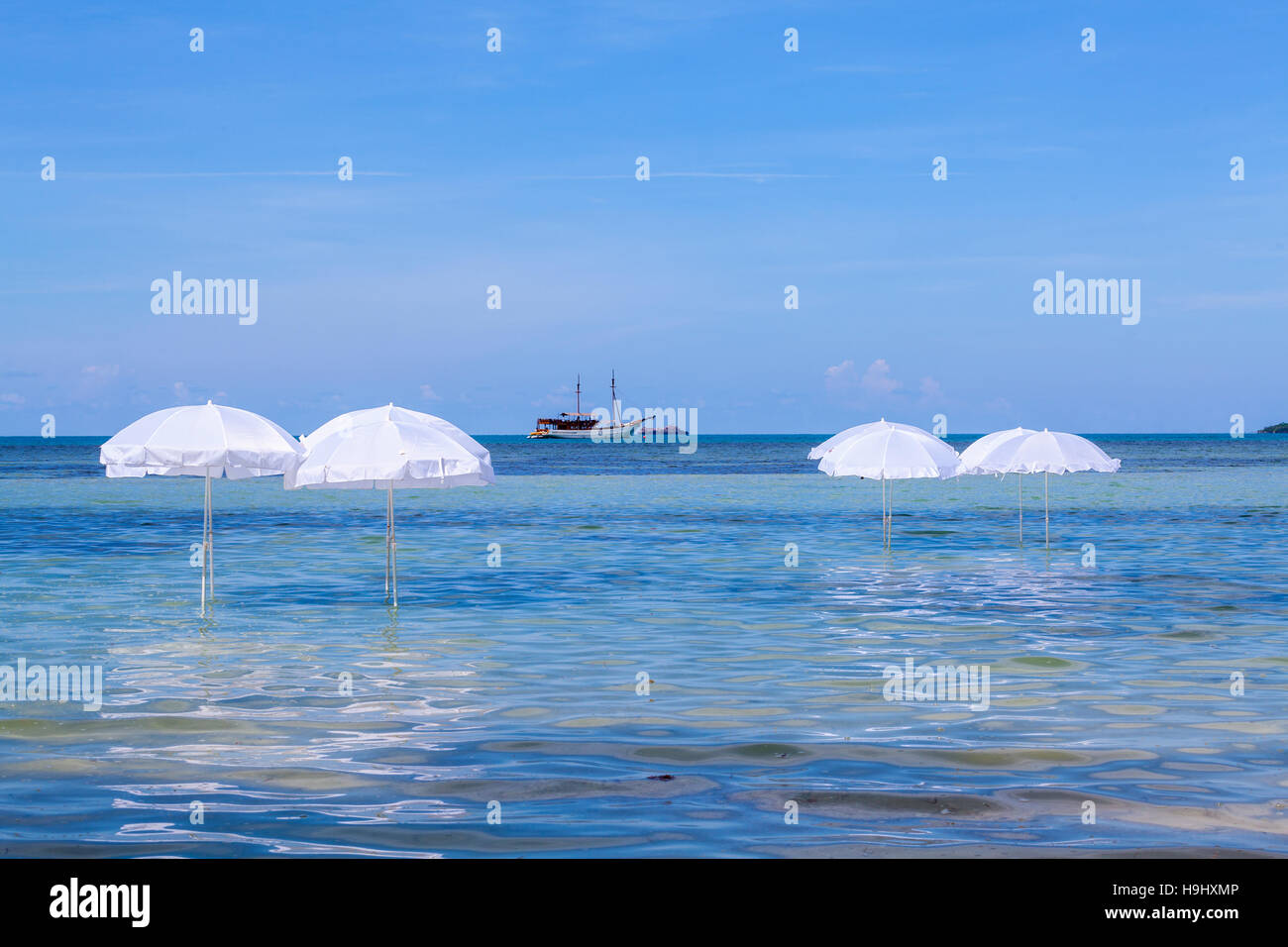 White umbrella on summer tropical beach with sailing boat Stock Photo