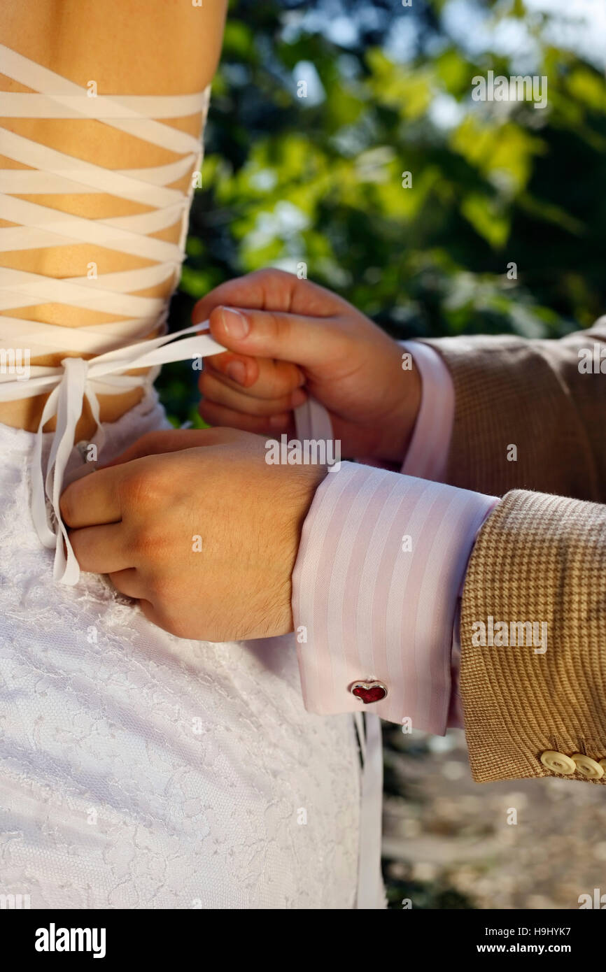 The groom helps the bride to tie a ribbon on the dress Stock Photo Alamy