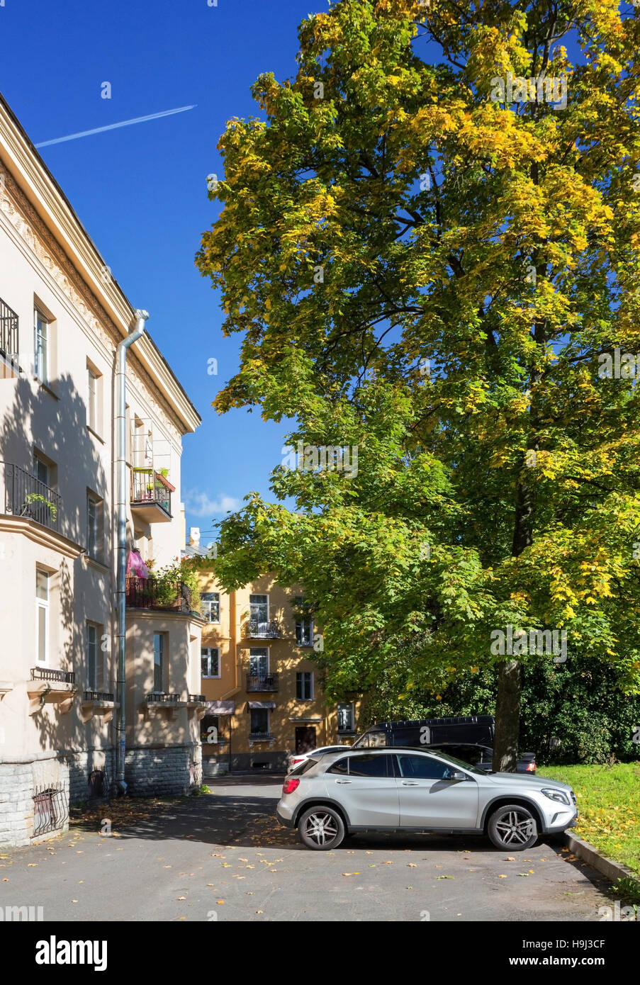 Car in the courtyard under the tree and the plane in the sky at sunny autumn day. Stock Photo