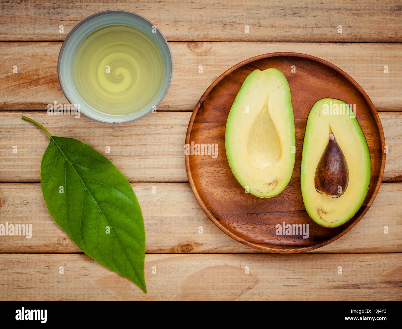 Fresh avocado with avocado leaves and oil on wooden background. Stock Photo