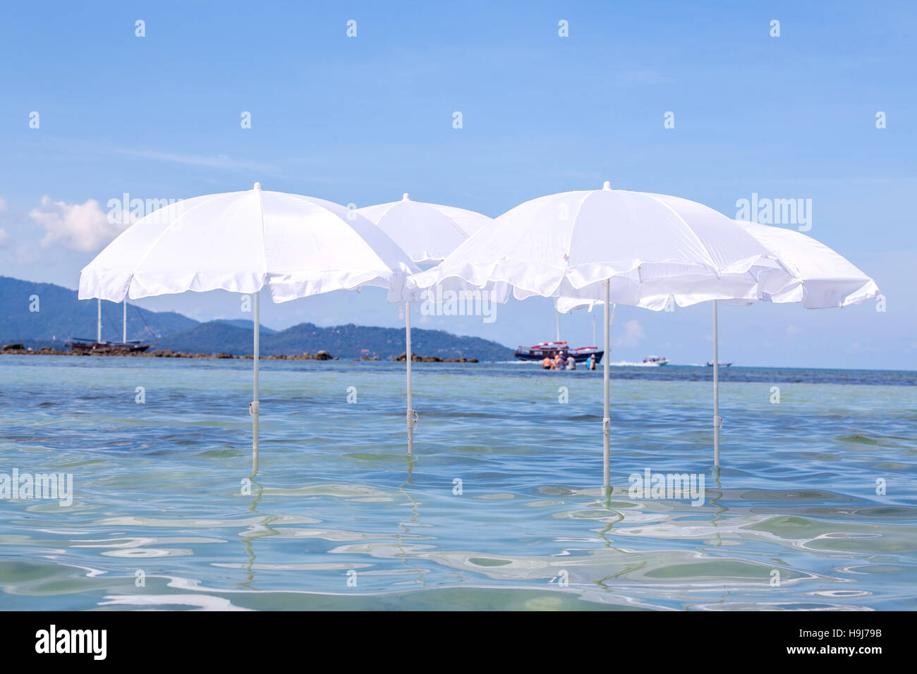White umbrella on summer tropical beach with sailing boat Stock Photo