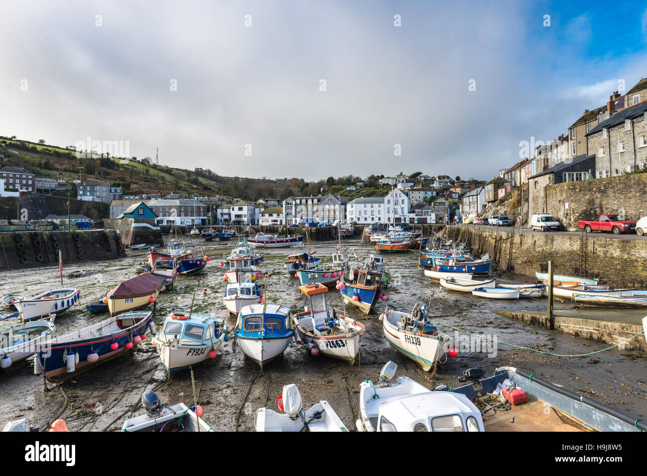 A pretty harbour of fishing boats surrounded by buildings in Mevagissey, Cornwall under a threatening sky. Stock Photo