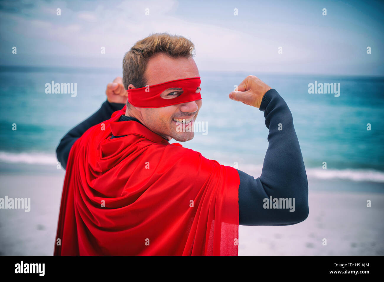 Man in superhero costume flexing muscles at sea shore Stock Photo