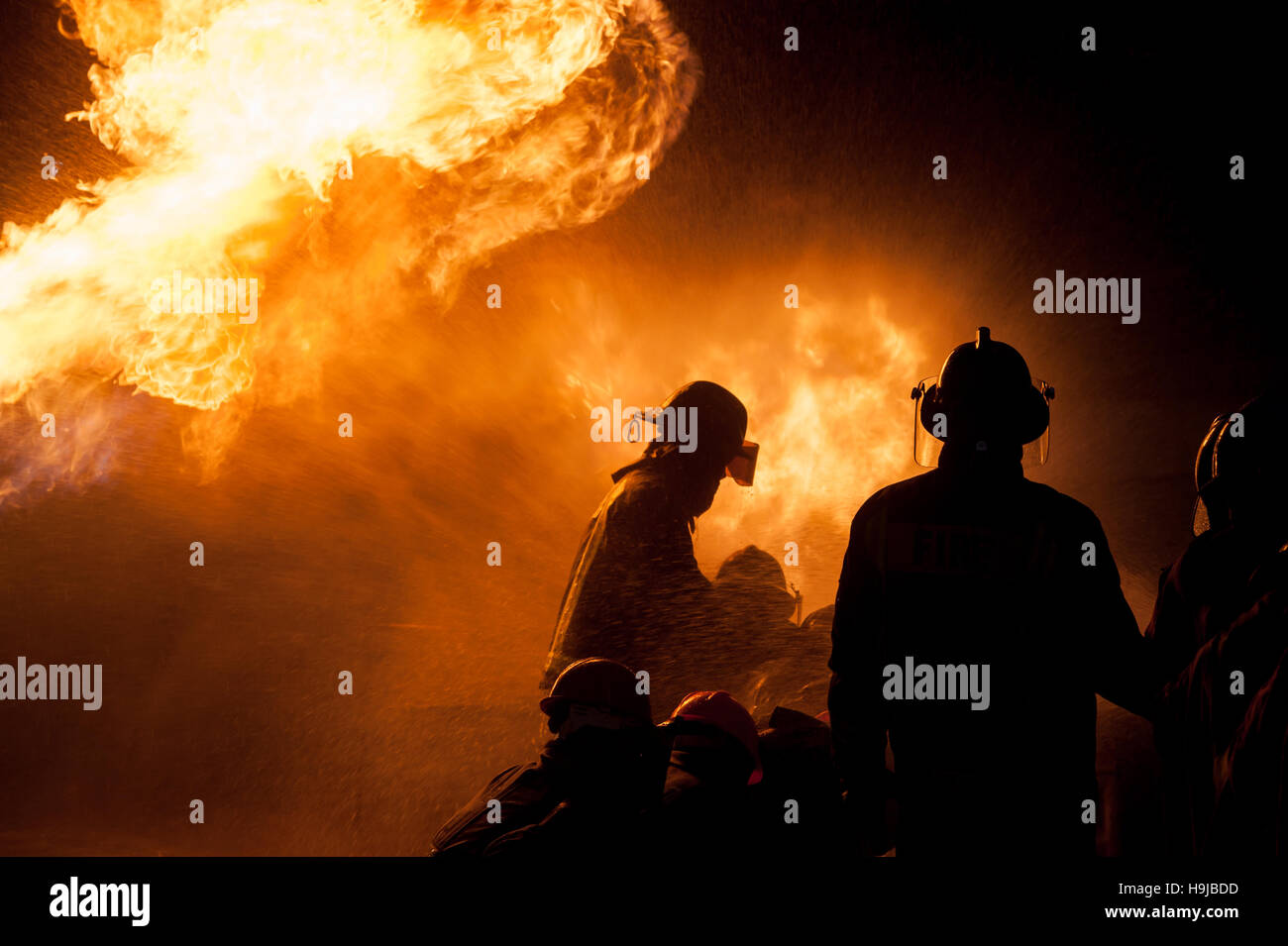 Silhouette of Firemen fighting a raging fire with huge flames of ...