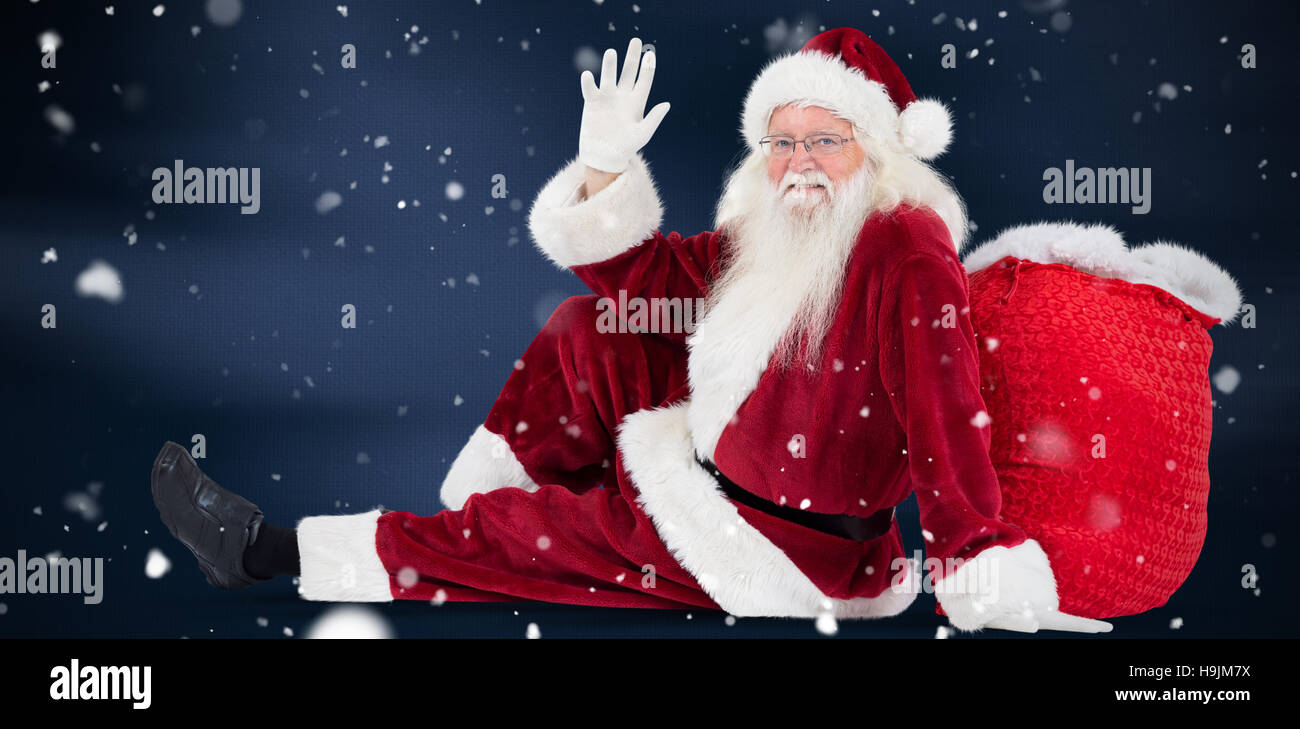 Composite image of santa sits leaned on his bag and waves Stock Photo