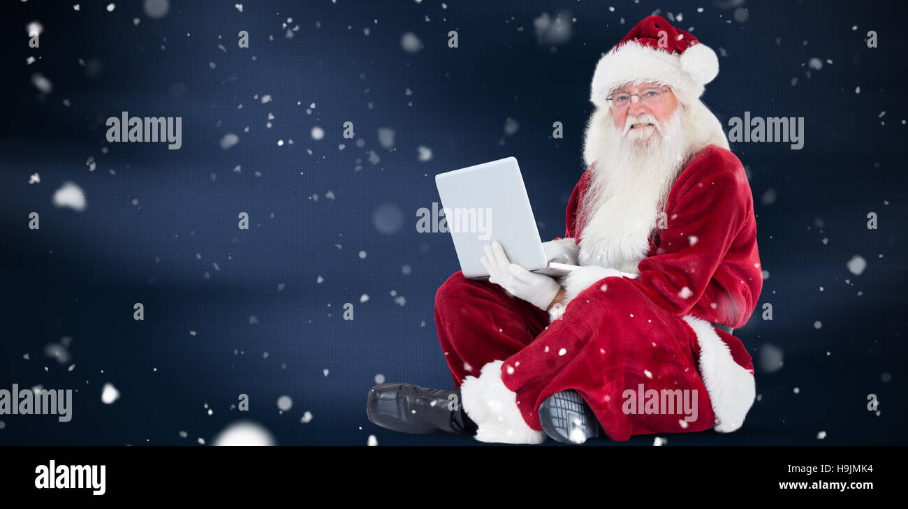 Composite image of santa sits and uses a laptop Stock Photo