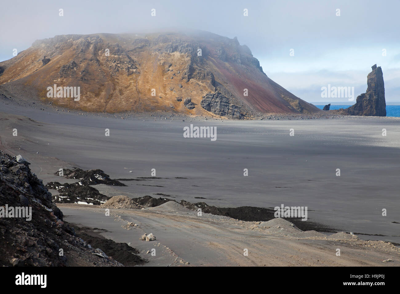 Rhyolite mountain and volcanic plug / volcanic neck / lava neck on beach of Jan Mayen, island in the Arctic Ocean in spring Stock Photo