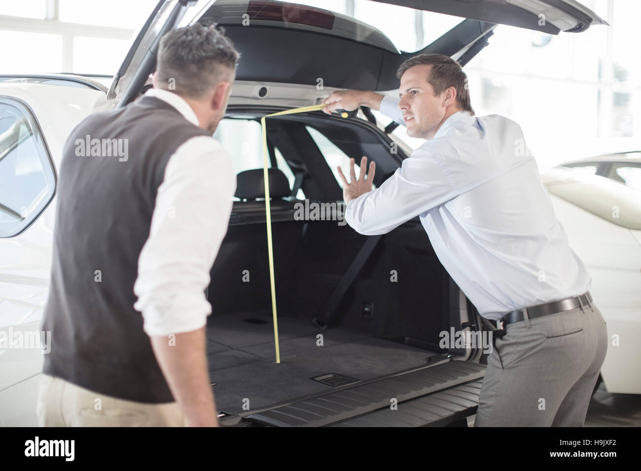 Car dealer opening hatchback of car to customer at car dealership Stock