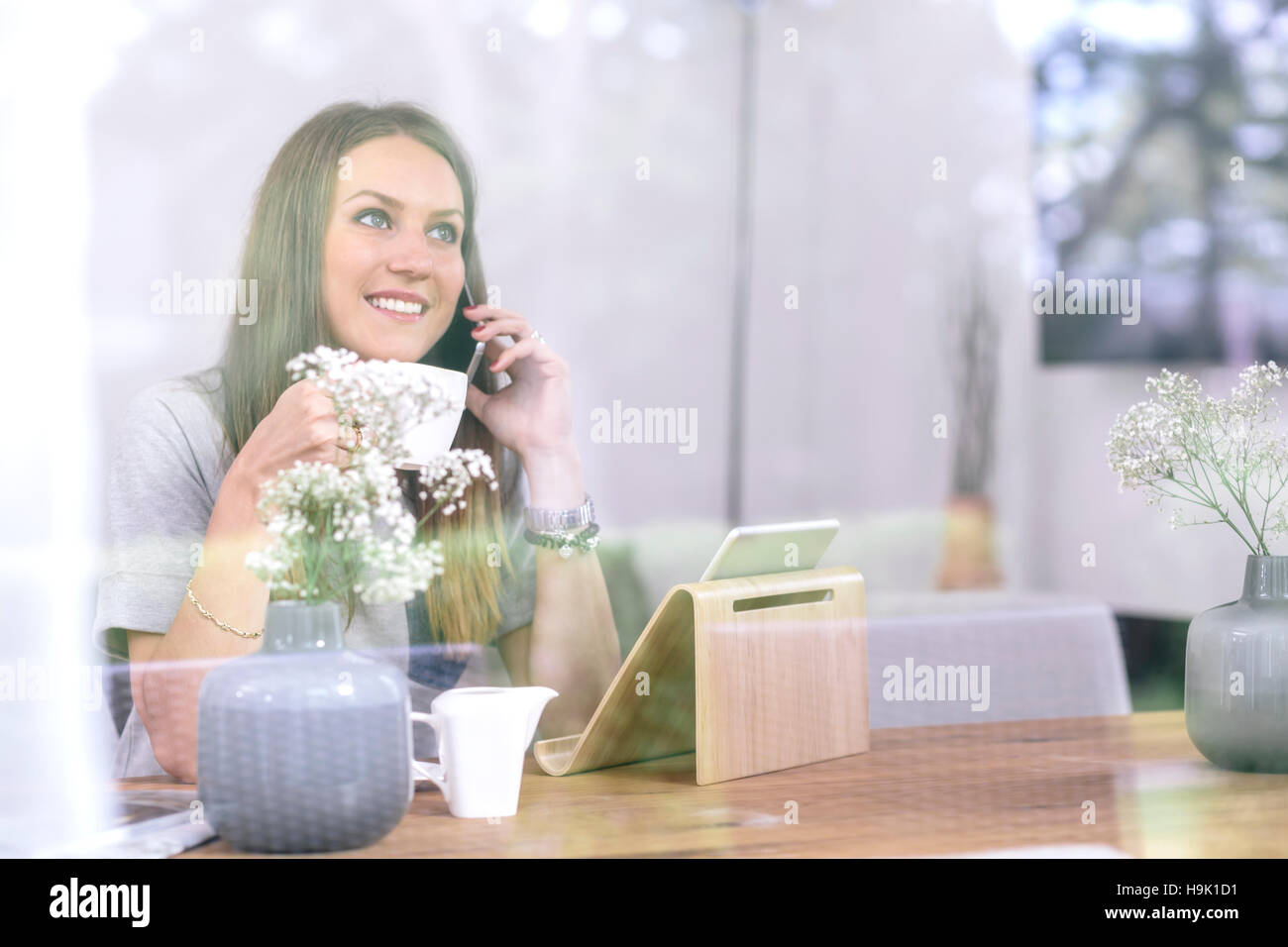 Smiling young woman at home using cell phone and tablet Stock Photo