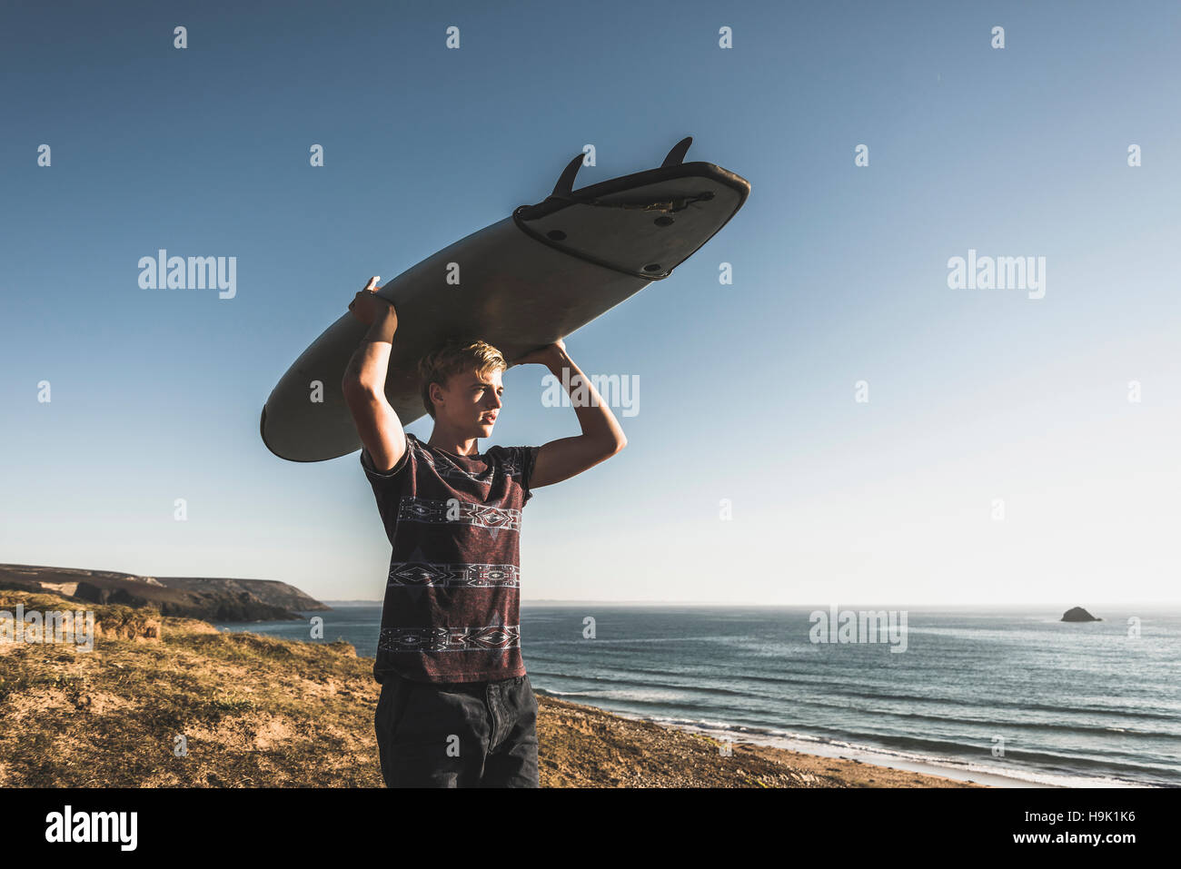 Teenage boy carrying surfboard on head Stock Photo