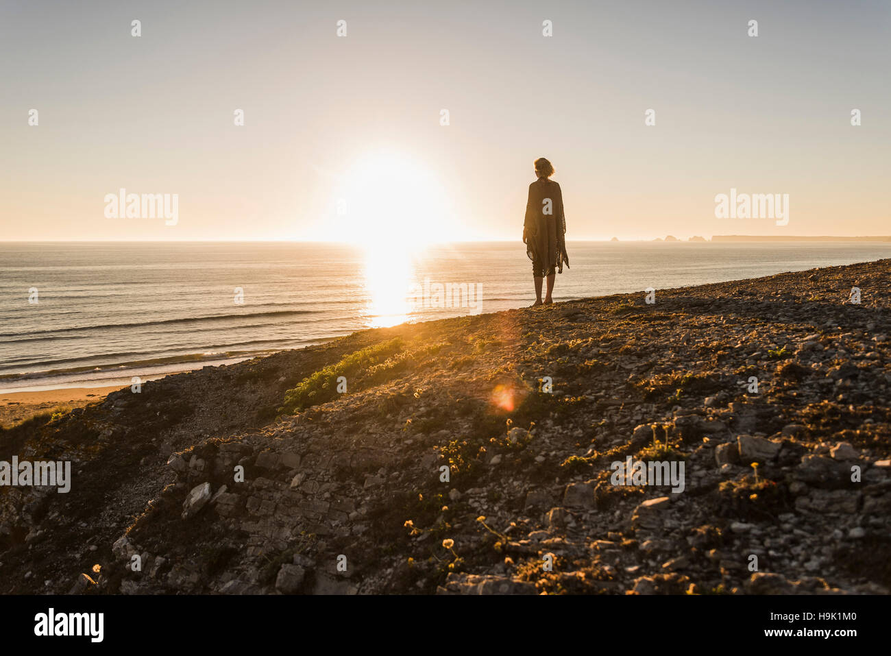 Back view of teenage girl standing on hill at sunset looking to the sea Stock Photo