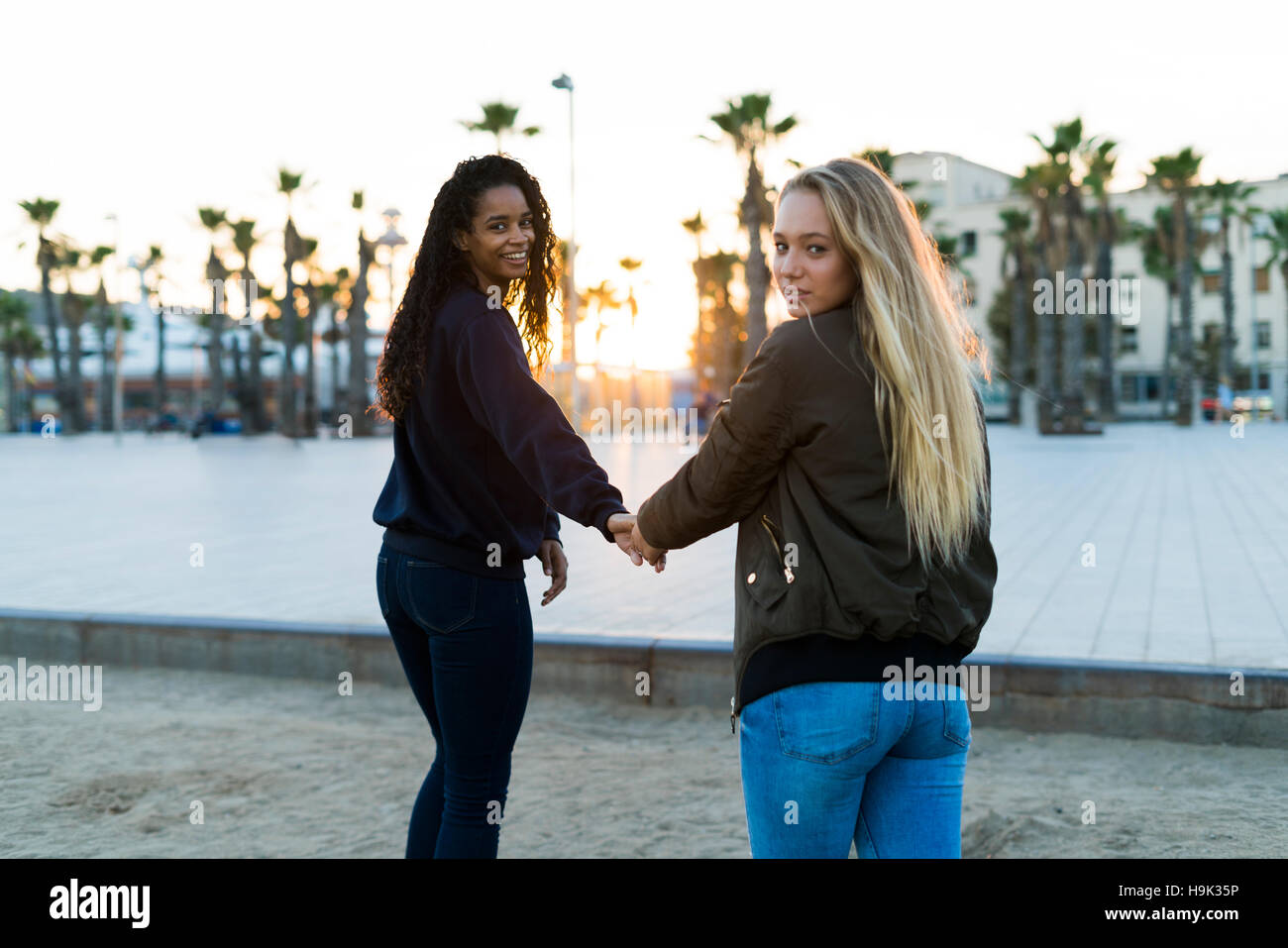 Two young women walking hand in hand at sunset Stock Photo - Alamy