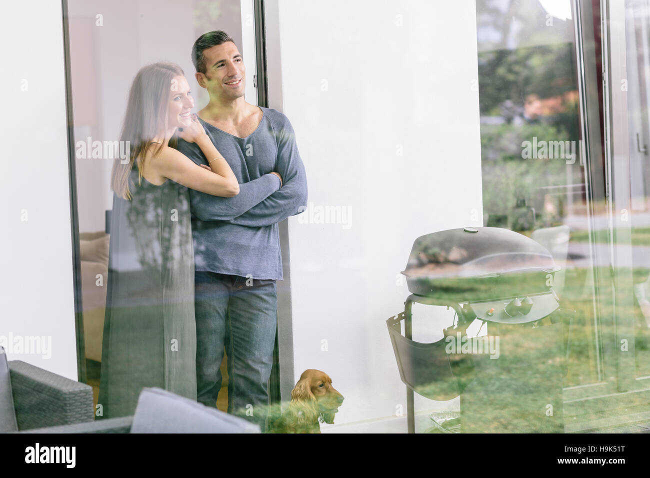 Smiling couple with dog standing at terrace door Stock Photo