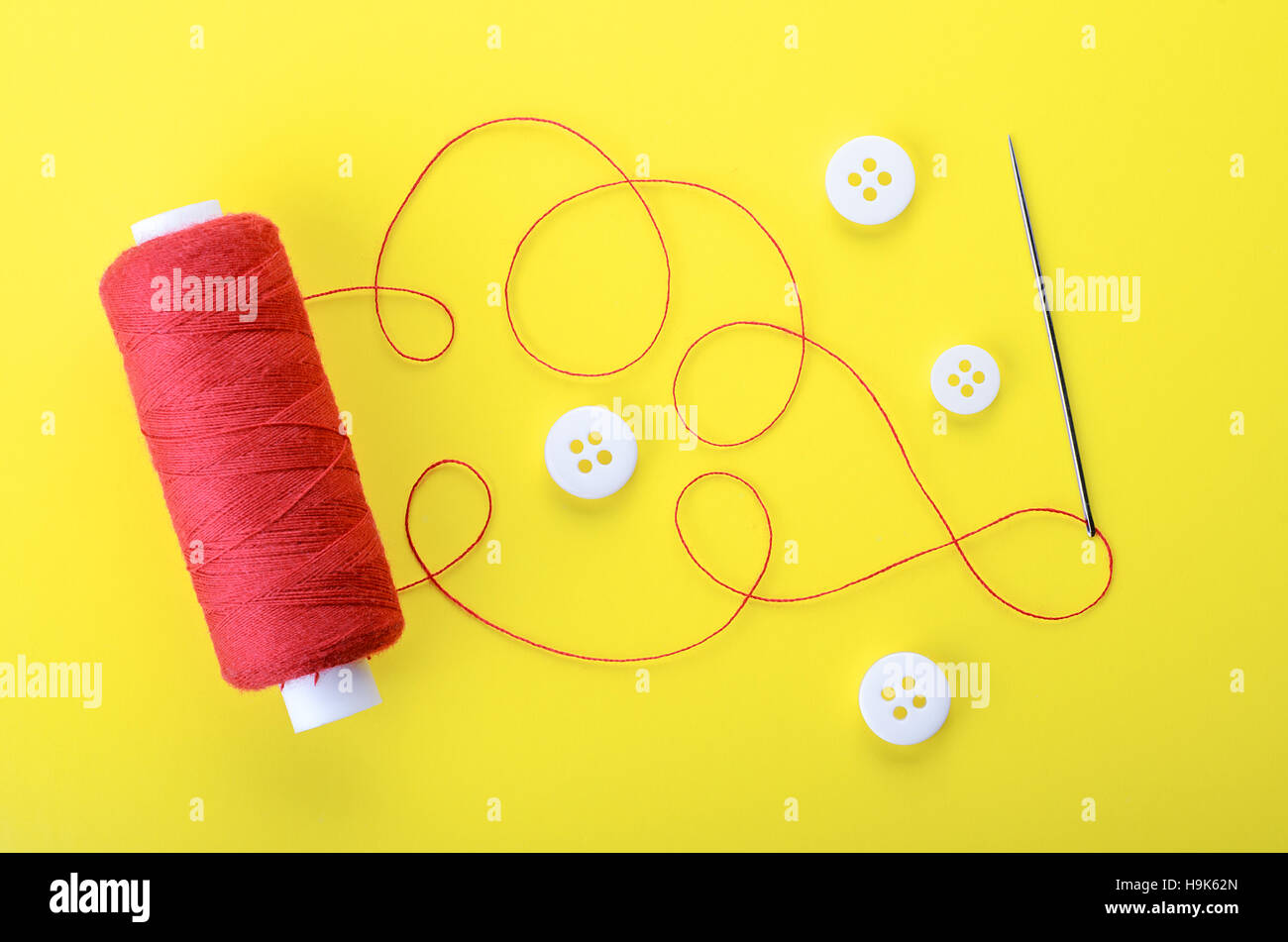 Spool of red thread, needle and clothing buttons on yellow background,  symbol of handmade and needlework. Stock Photo