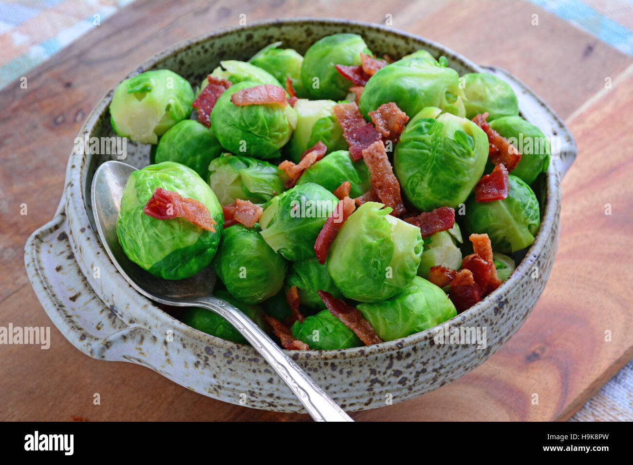 Fresh steamed brussels sprouts with crisp bacon bits in speckled serving dish. Shot in natural light in horizontal format. Stock Photo