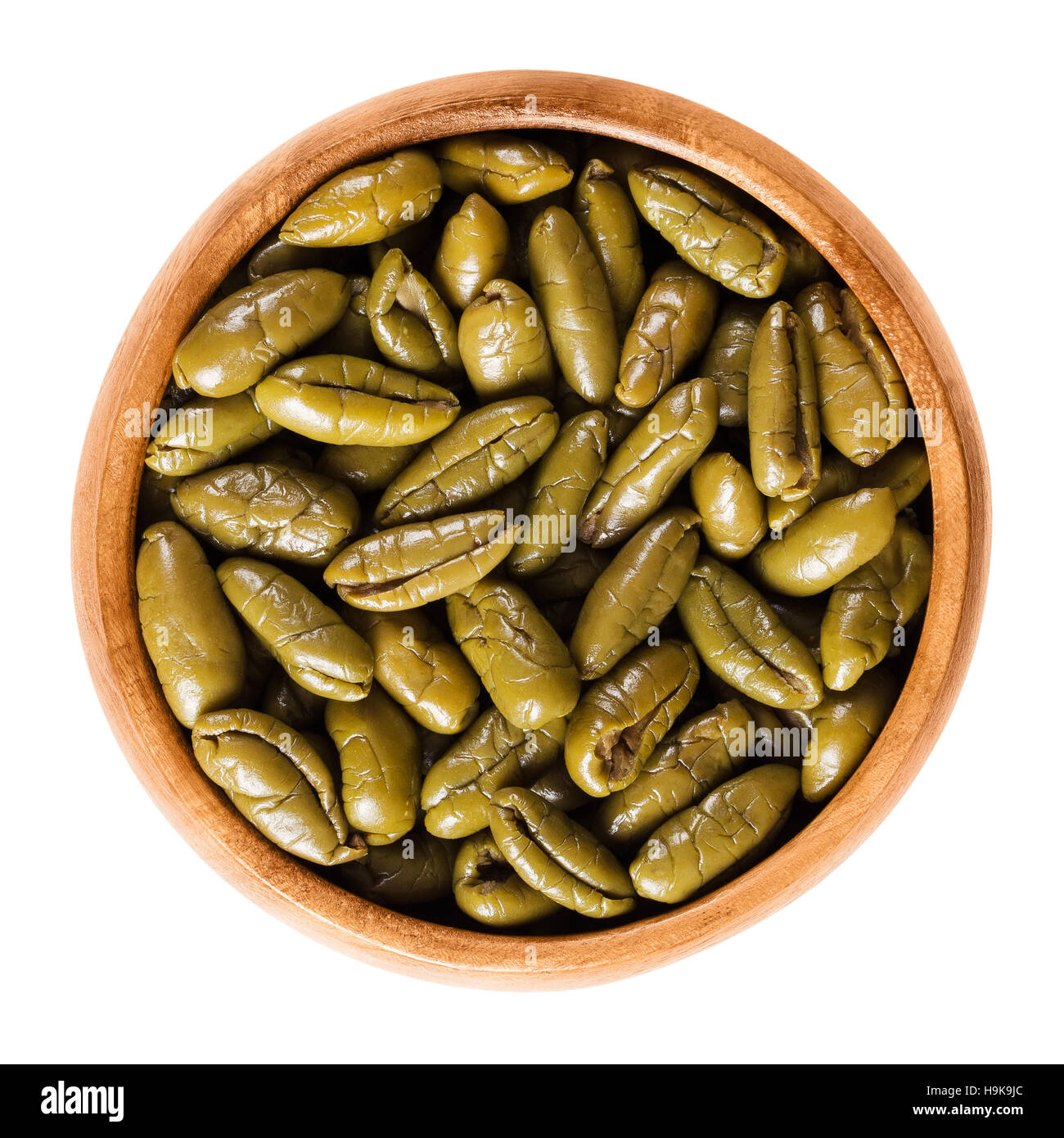 Dried green olive halves in a wooden bowl. Half table olives, dried ripe fruits of Olea europaea. Isolated macro food photo. Stock Photo