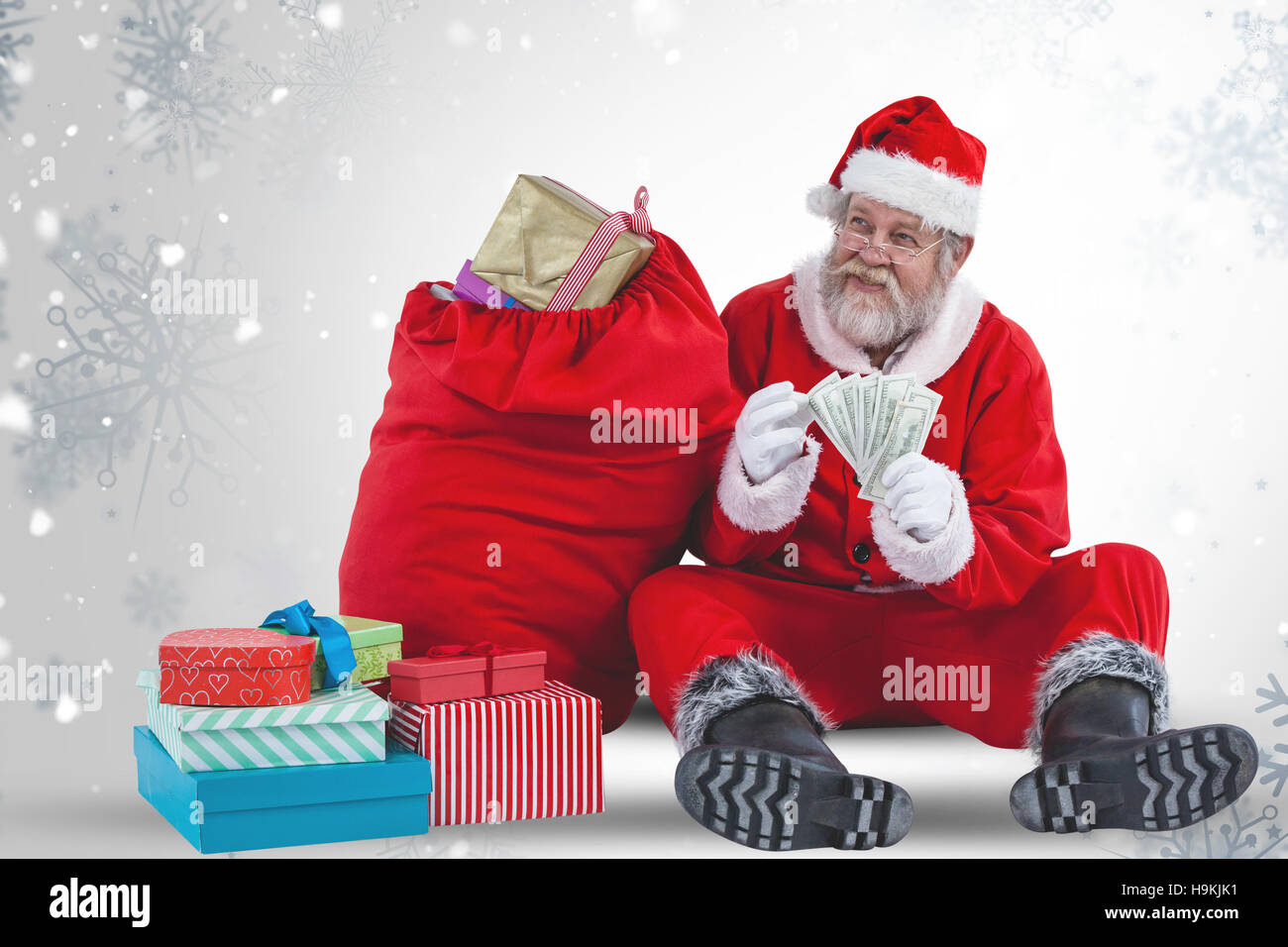 Composite image of santa claus sitting by christmas gifts and counting currency notes Stock Photo