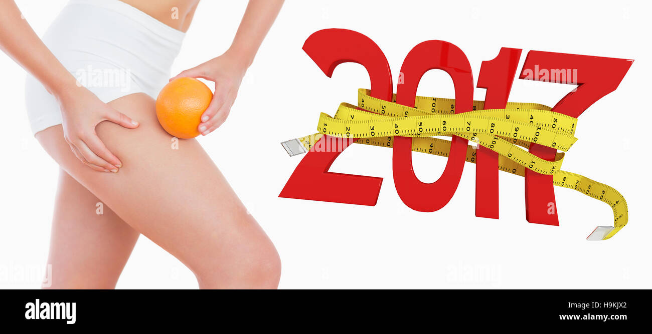 3D Composite image of fit woman squeezing fat on thigh as she holds orange Stock Photo