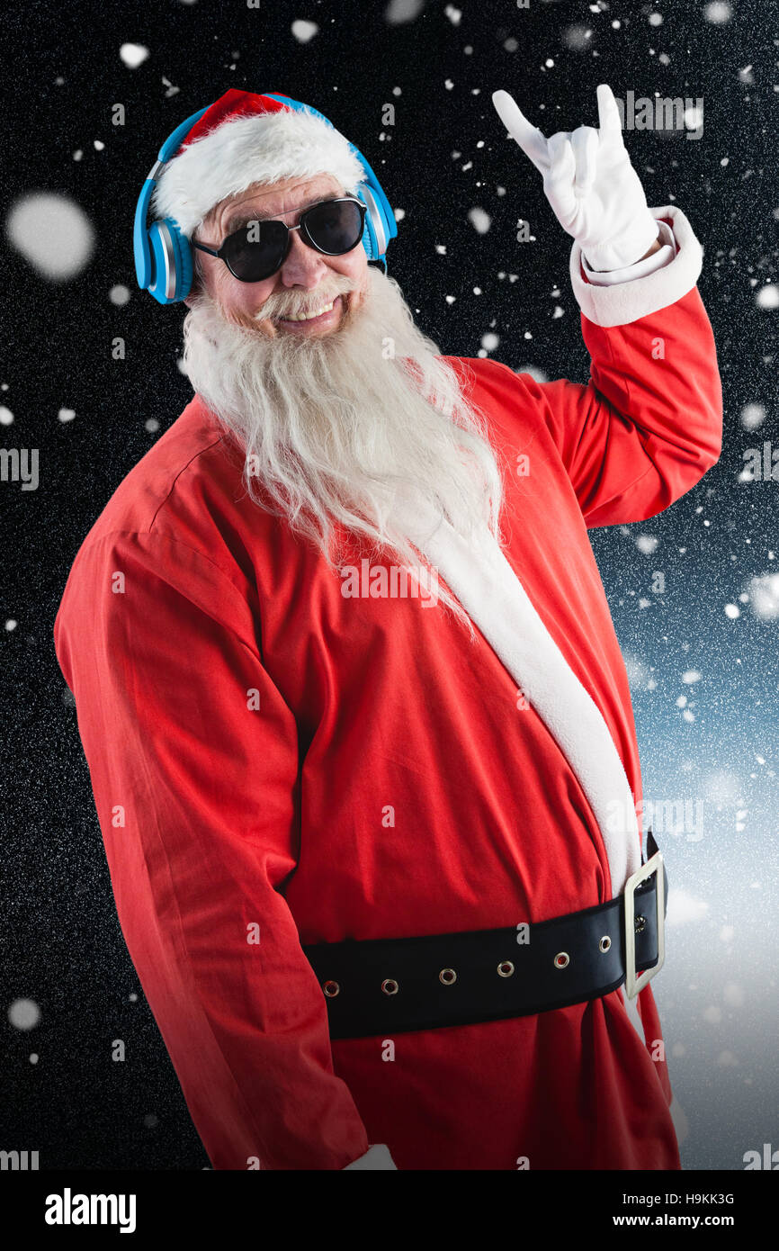 Composite image of santa claus showing hand yo sign while listening to music on headphones Stock Photo