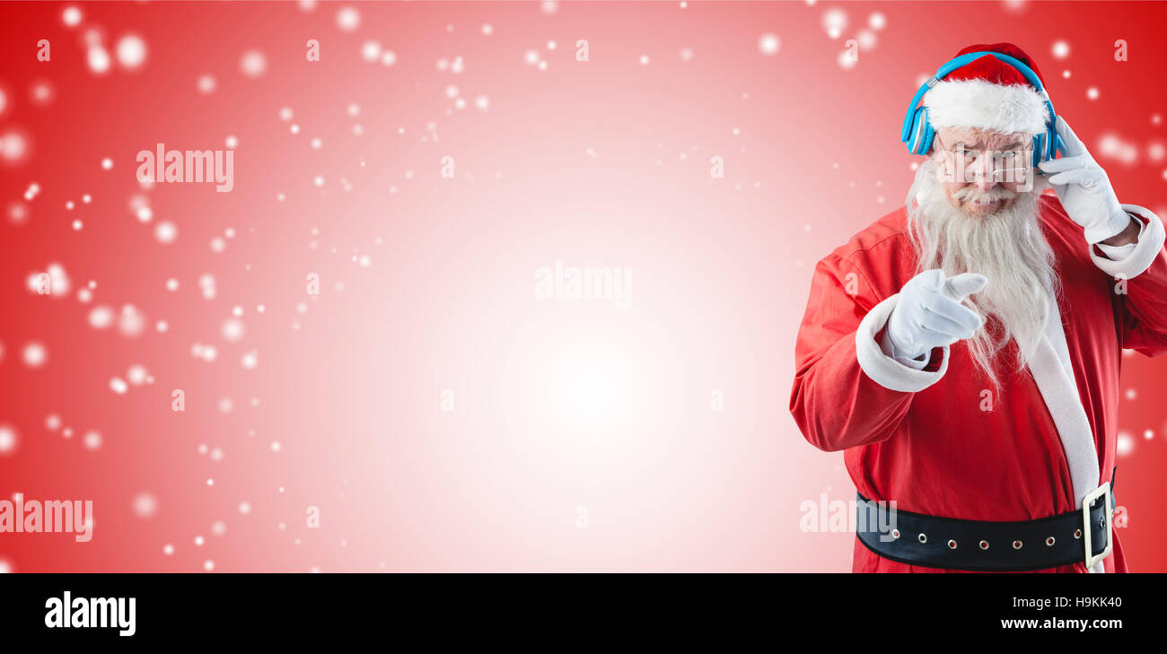 Composite image of portrait of santa claus listening to music on headphones while pointing Stock Photo