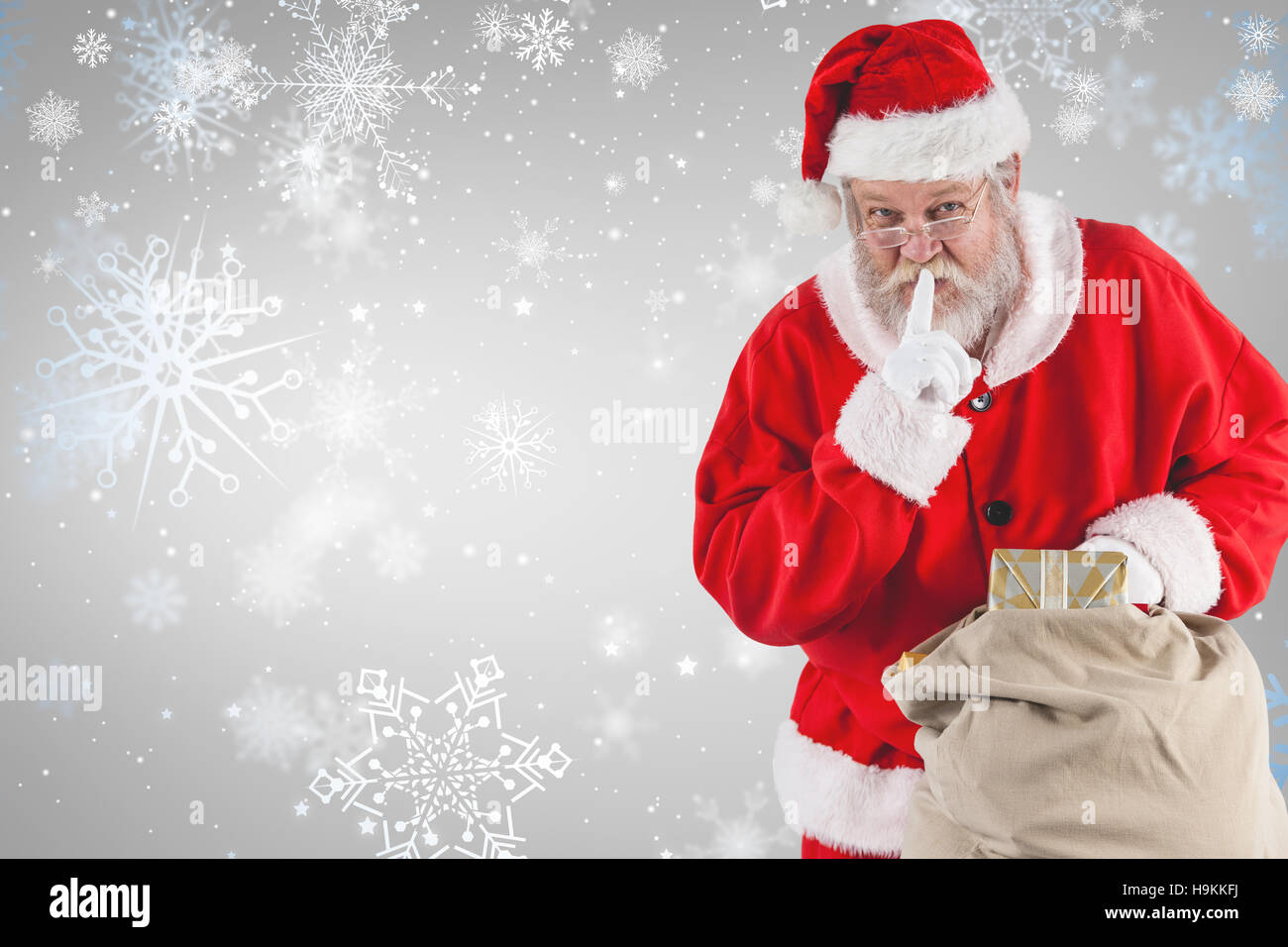 Composite image of santa claus with finger on lips and holding gifts Stock Photo