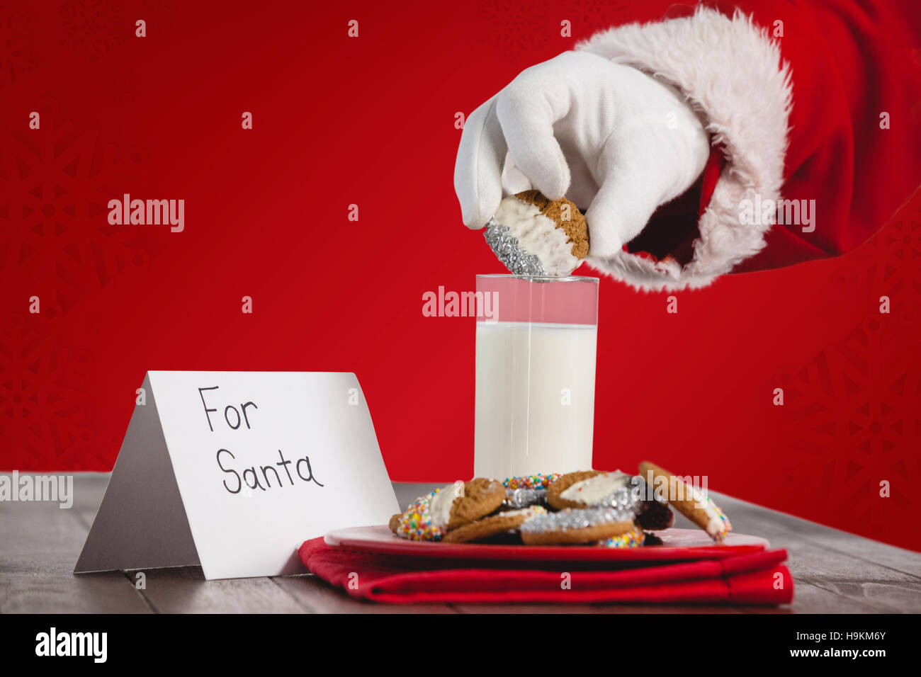 Composite image of cropped image of santa claus dipping cookies in glass of milk Stock Photo