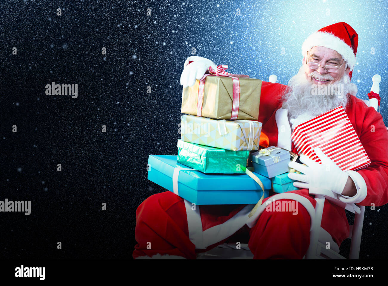 Composite image of portrait of cheerful santa claus holding christmas presents on chair Stock Photo